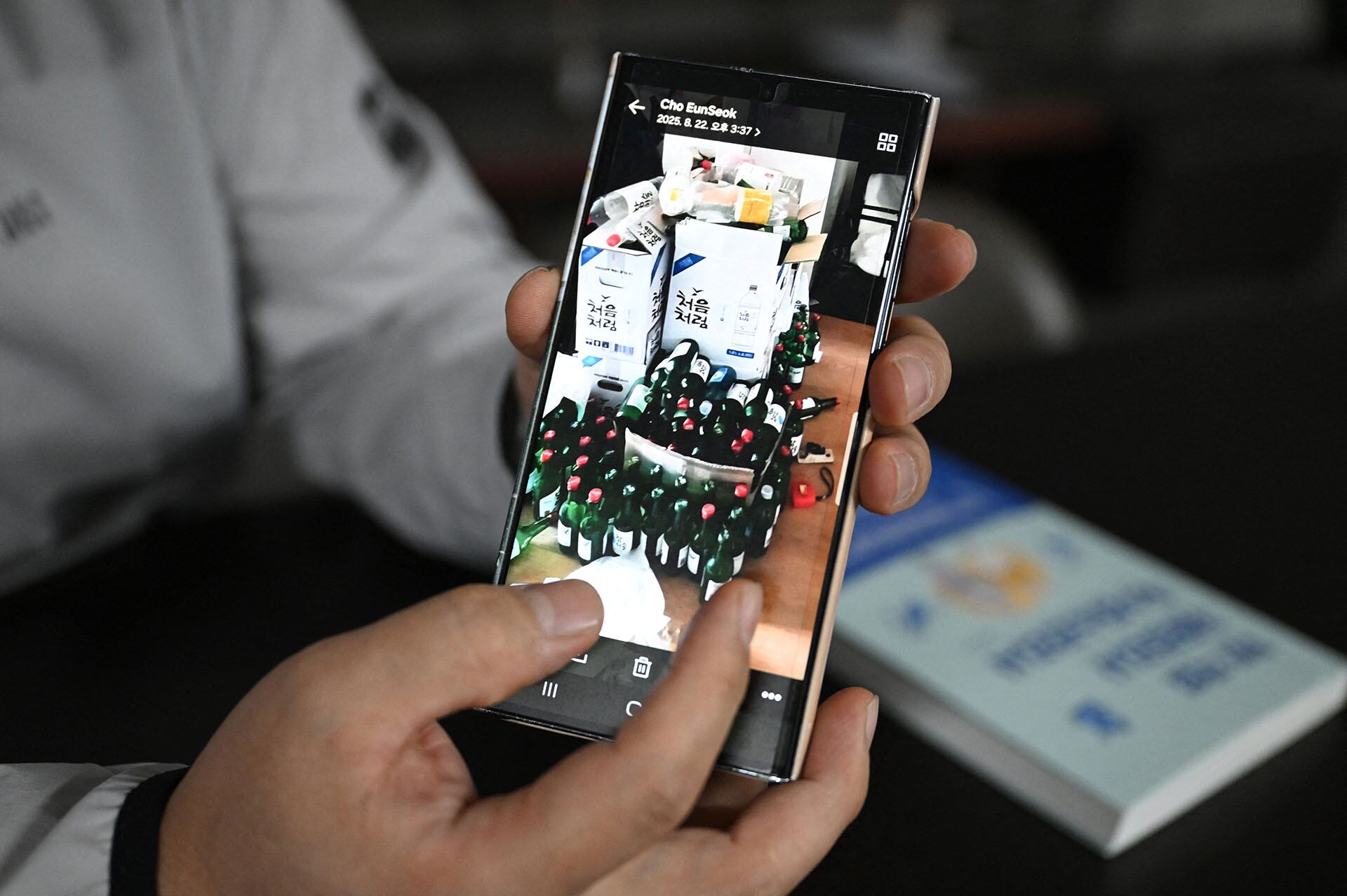 Cho Eun-seok, un limpiador que ordena casas tras el fallecimiento de sus ocupantes —a menudo personas que vivían solas—, muestra una fotografía de cientos de botellas de soju cuidadosamente tapadas en la habitación de una persona fallecida durante una entrevista con la AFP en su oficina de Guri. (Foto de Jung Yeon-je / AFP)