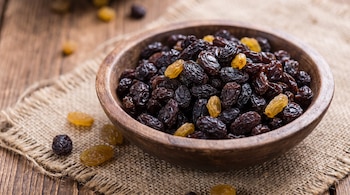 Un cuenco de madera con uvas pasas oscuras y doradas sobre un paño de arpillera y una mesa.