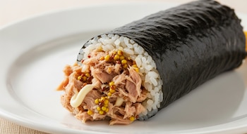 Primer plano de un rollo de Chamchi Gimbap sobre un plato blanco. Se aprecian el arroz, el atún desmenuzado, granos de mostaza y un toque de mayonesa.