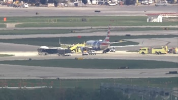 Un avión comercial detenido en una pista asfaltada junto a autobuses y vehículos de emergencia amarillos en un aeropuerto