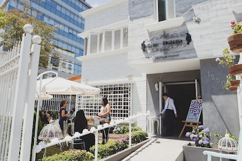 Vista exterior de Las Bolena Tea Room & Restaurant con fachada blanca y gris, área de terraza con sombrillas y personas, y un miembro del personal en la entrada