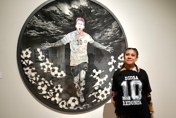 Mujer con trenzas y camiseta negra frente a un cuadro redondo de Lionel Messi con camiseta número 10, rodeado de balones de fútbol