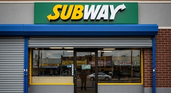 Fachada frontal de un local de Subway cerrado, con su logo verde y amarillo prominente, persianas metálicas bajadas y un cartel de "Closed" en la puerta de cristal.