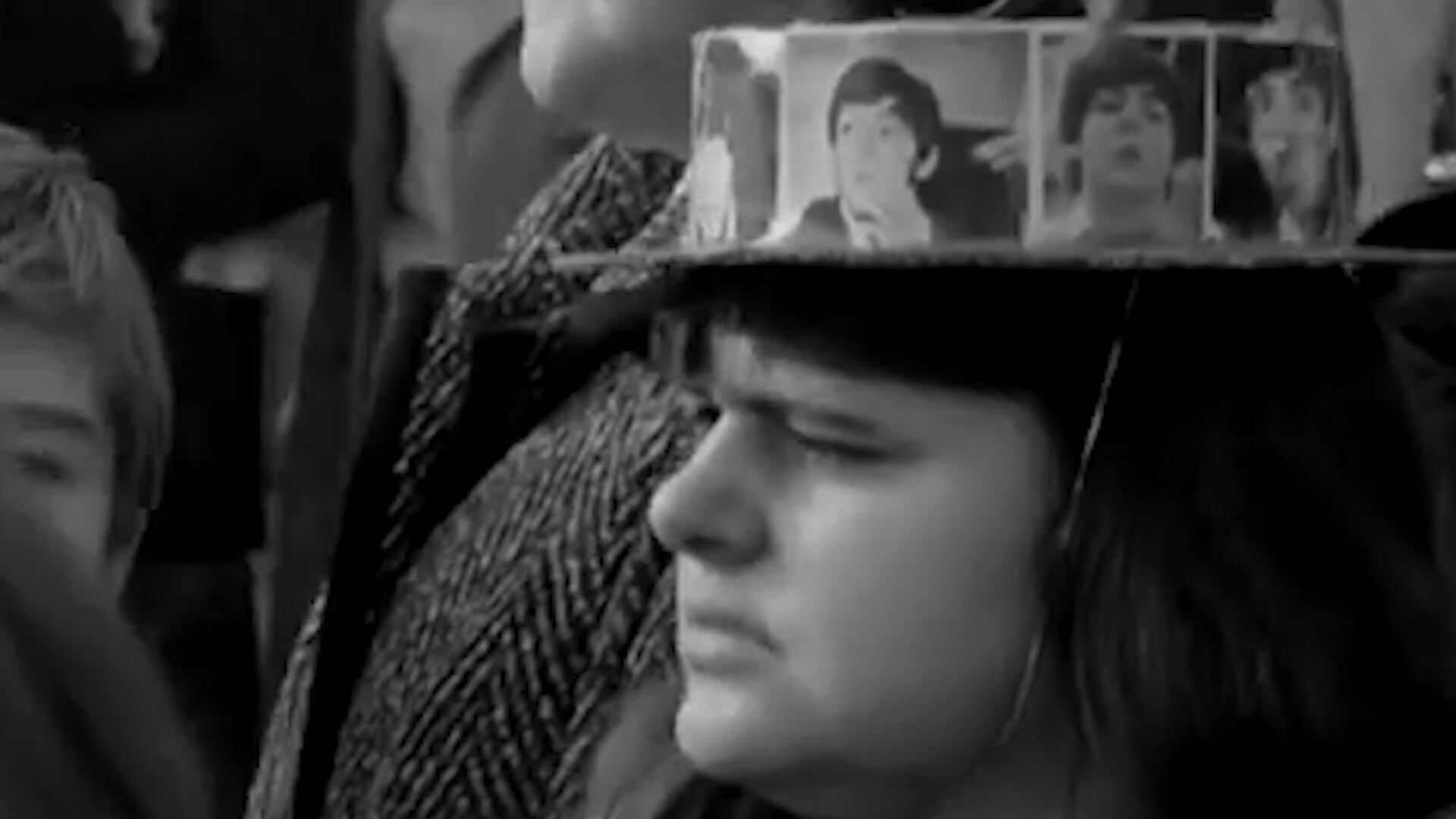 Una joven con un sombrero decorado con las caras de los cuatro de Liverpool en la puerta del Palacio de Buckingham