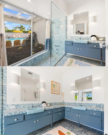 Vistas de un baño con muebles azules, lavabos celestes, espejos, ducha de vidrio y un ventanal hacia un patio con piscina