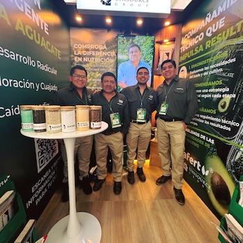 Cuatro hombres posan en un stand de exposición con seis frascos de productos granulados y carteles con el logo Unisource Group