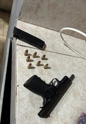 Una pistola negra, un cargador, siete balas y un cable blanco sobre una superficie de baldosas de color claro