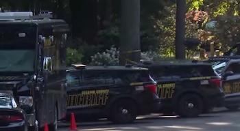 Tres vehículos negros del sheriff del condado de Ottawa, luces de emergencia, cinta policial amarilla atada a un árbol y conos naranjas en el suelo