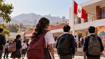 Estudiantes con uniformes escolares y mochilas caminan en el patio de un colegio frente a la bandera peruana y colinas al fondo
