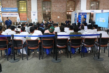 Funcionarios en uniforme azul atienden a personas frente a computadoras y sellos junto a un cartel del Instituto Guatemalteco de Migración