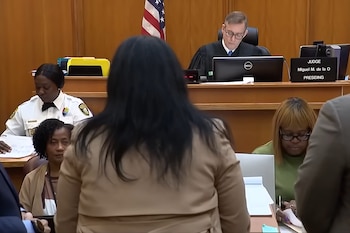 Vista trasera de una persona con cabello oscuro en un tribunal; el juez Miguel M. de la O está sentado al fondo, con una bandera de EE. UU. detrás
