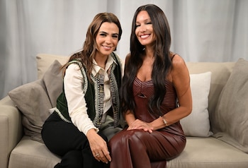Agustina Cherri, con blusa blanca y chaleco verde bordado, y Pampita, con un vestido marrón rojizo, sentadas en un sofá claro, sonriendo a cámara
