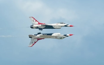 Dos F-16 Fighting Falcon de los Thunderbirds, uno derecho y el otro invertido, con esquemas de pintura rojo, blanco y azul, contra un cielo azul claro