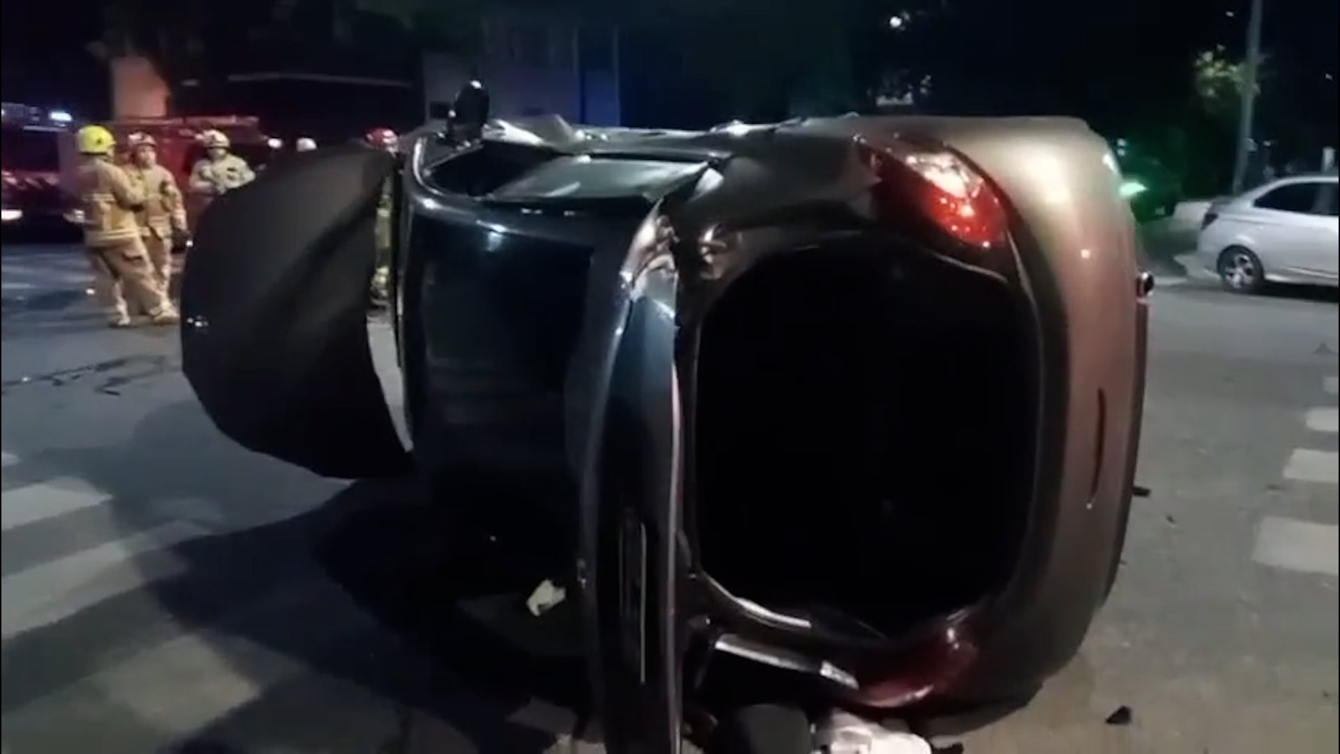 Un vehículo oscuro volcó sobre su lateral en Barracas, mientras bomberos trabajan en la escena de un accidente de tránsito.