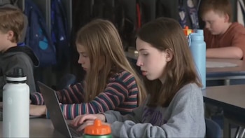 Estudiantes sentados en un aula escolar utilizan computadoras portátiles sobre sus escritorios