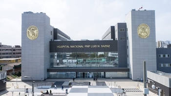 Edificio de hospital moderno con nombre Hospital Nacional PNP Luis N. Sáenz en la fachada, dos emblemas dorados en torres laterales, y personas afuera
