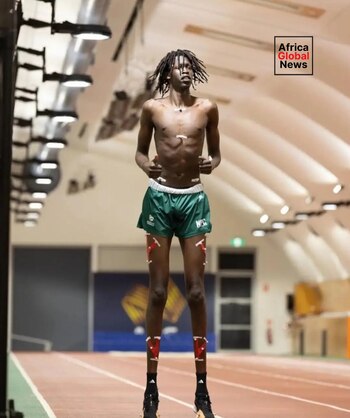 Hombre de piel oscura y rastas, sin camiseta, con shorts verdes, calcetines negros y zapatillas, sobre pista de atletismo. Sensores en torso y piernas