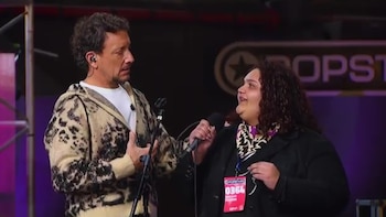 Nico Vázquez coloca su mano sobre el pecho frente a una participante con un micrófono y una credencial de Popstars
