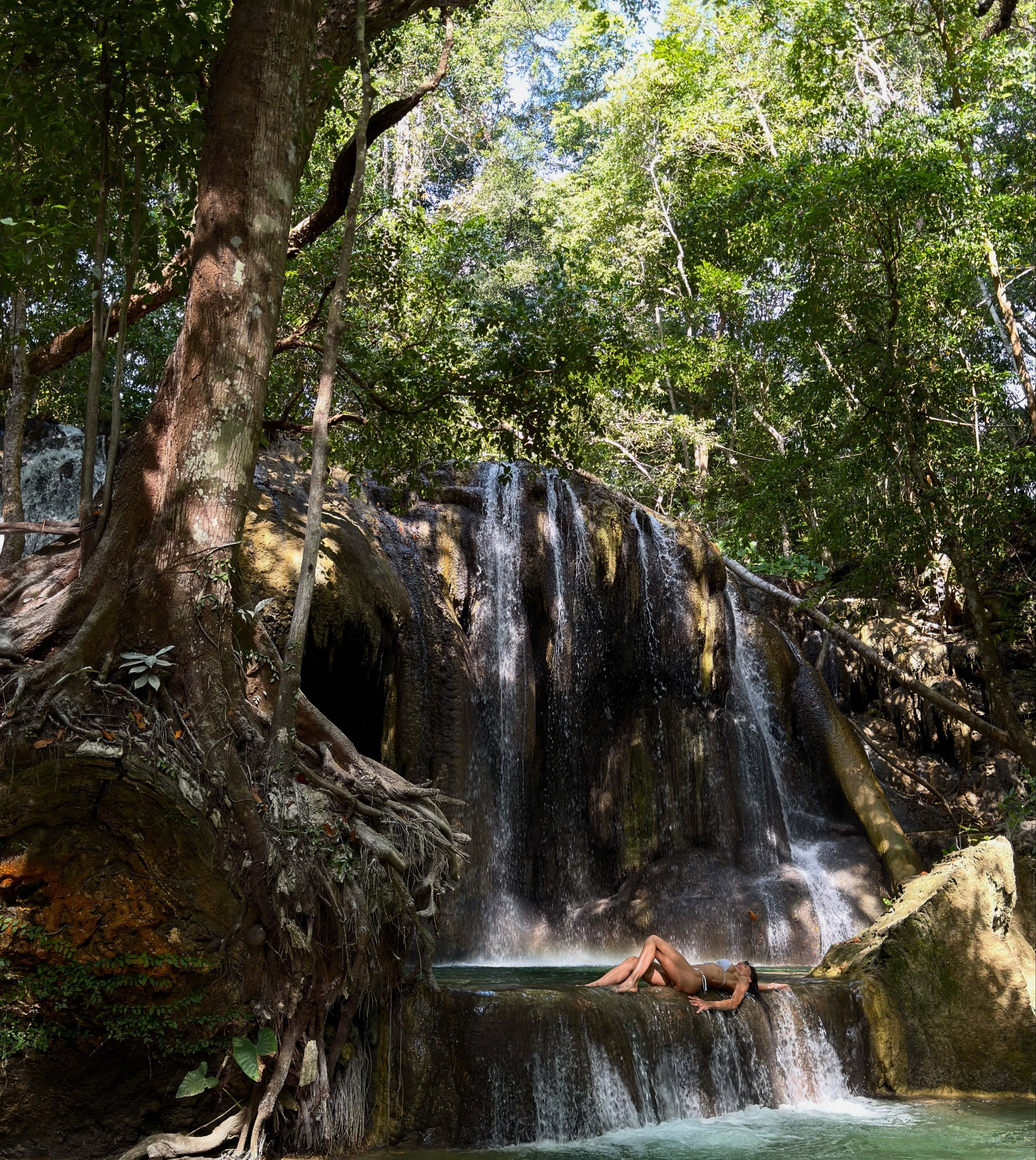 María recostada sobre una formación rocosa al pie de una cascada en un entorno natural