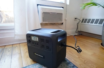 Estación de energía portátil Every Electric negra con pantalla digital y múltiples enchufes, conectada a la corriente en una habitación con piso de madera y un aire acondicionado