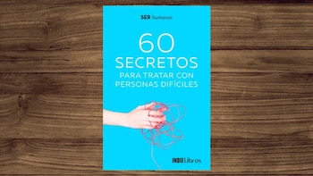 Cubierta de un libro azul brillante titulado "60 Secretos para tratar con personas difíciles", con una mano sujetando una cuerda roja enredada, sobre madera