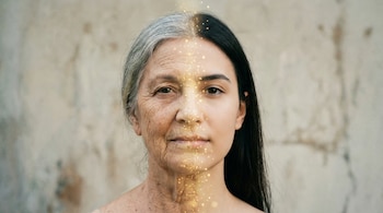 Retrato frontal de una persona cuya cara se divide verticalmente: la izquierda muestra rasgos de vejez y la derecha de juventud, unidas por luces doradas.