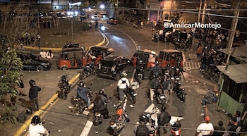 Mototaxis, motocicletas y automóviles detenidos en medio de una calle iluminada de noche con varias personas alrededor