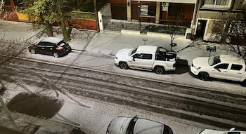 Vista nocturna desde lo alto de una calle cubierta de nieve con huellas de neumáticos y varios automóviles y camionetas estacionados