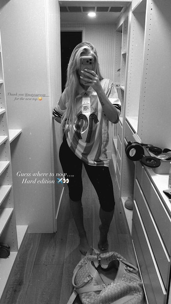 Mujer rubia toma selfie en un espejo. Viste camiseta de la selección argentina con número 10 y leggings negros. Está descalza en un vestidor