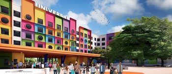 Edificio vibrante y multicolor del Parque Temático Universal Kids con ventanas variadas, personas caminando en la entrada, árboles frondosos y cielo azul con nubes