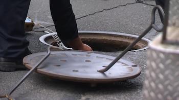 Una persona manipula el interior de una alcantarilla abierta en la calle utilizando palancas de metal