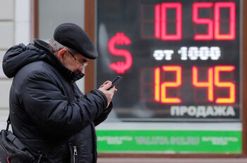 Un hombre mira su celular con un cartel de la cotización del rublo frente al dólar en San Petesburto (REUTERS/Anton Vaganov)