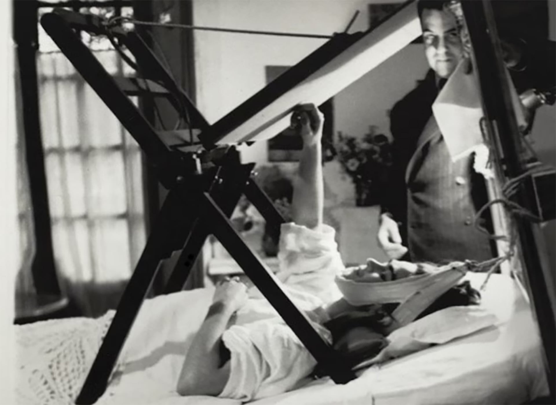 Frida Kahlo pinta recostada en su cama mediante una estructura de madera adaptada a sus necesidades de reposo luego del grave accidente. En la foto aparece Diego Rivera