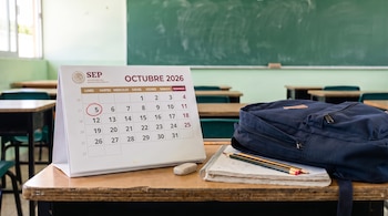Calendario de escritorio de la SEP en octubre de 2026, cuaderno con lápices y mochila sobre un pupitre frente a un pizarrón.