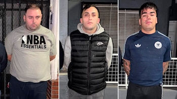 Tres hombres jóvenes de pie, con las manos detrás de la espalda, posan para una foto policial. El tercero, a la derecha, presenta sangre en la cara