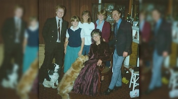 Seis personas, entre adultos y jóvenes, sonríen junto a dos perros, uno blanco y negro y otro dorado, en una sala.