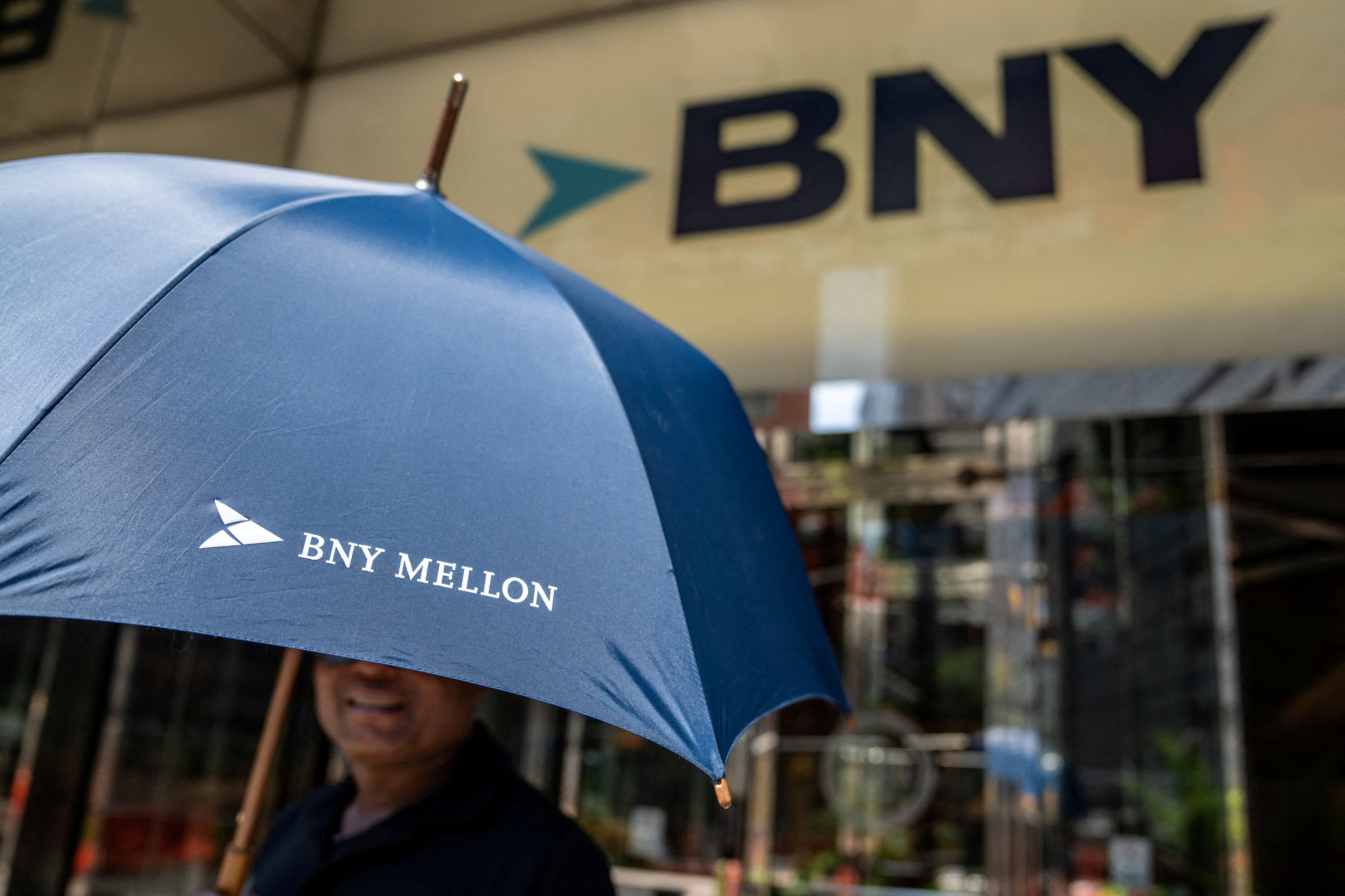 FILE PHOTO: A person holds an umbrella with the logo of BNY Mellon near the offices of BNY Mellon investment banking company in New York City, U.S., July 10, 2024.REUTERS/David