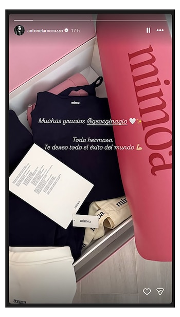 Vista superior de una caja de regalo rosa y blanca que contiene ropa oscura y clara de la marca Mimooa, una etiqueta y una tarjeta con texto