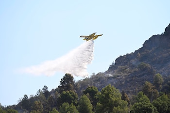Una avioneta de la lucha contra el fuego descarga agua para la extinción del incendio forestal de Soneja (Castellón).