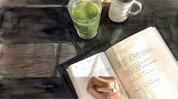 Vista superior en acuarela de una mano que escribe con bolígrafo en una libreta sobre una mesa de madera junto a un vaso verde y una taza
