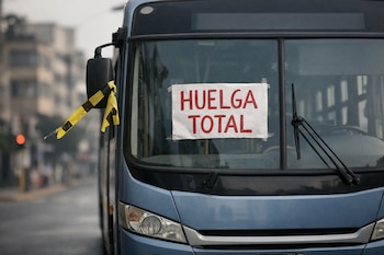 Primer plano de un autobús urbano azul detenido, con un cartel de 'Huelga total' en el parabrisas y cinta amarilla en el espejo retrovisor.