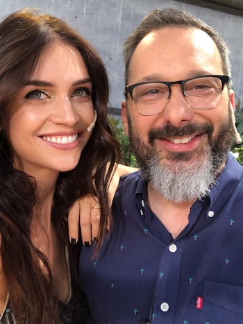 Primer plano de Zaira Nara y Gerardo Rozín sonriendo a cámara. Ella tiene cabello castaño oscuro y él barba gris, gafas y camisa azul