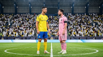 Cristiano Ronaldo vestido de amarillo y Lionel Messi de rosa permanecen de pie frente a frente en el centro del campo ante una multitud.
