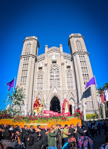 Una carroza procesional con estatuas religiosas de Jesús montado en un burro y otra figura. El conjunto está decorado con flores rojas, follaje y palmas