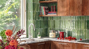 Vista detallada de una cocina ilustrada con técnica de acuarela, presentando paredes de azulejos verdes, muebles de madera, un fregadero, electrodomésticos y un jarrón con flores.