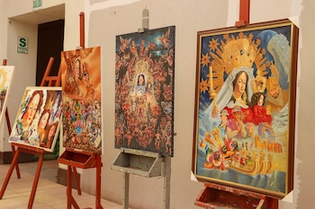 Pinturas colocadas sobre caballetes con representaciones de la Virgen María y danzantes tradicionales en un pasillo interior