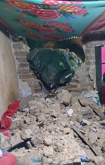 Una gran roca de color oscuro ha atravesado una pared de ladrillos, dejando un agujero y un montón de escombros de tierra y ladrillos en el suelo de una habitación