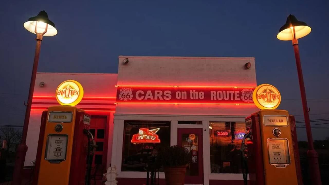 Una estación de servicio retro a lo largo de la histórica Ruta 66 brilla con luces de neón rojas al anochecer, flanqueada por bombas de gasolina vintage y farolas clásicas. (AP)