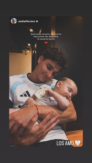 Primer plano de un hombre con camiseta de Argentina abrazando a un bebé dormido con chupete. El hombre tiene una pulsera roja