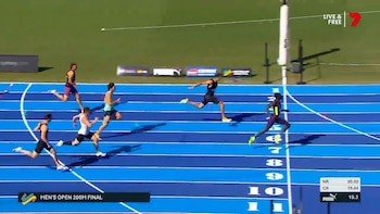 Vista aérea de seis atletas masculinos corriendo en una pista de atletismo azul bajo el sol, con el corredor Gout Gout visiblemente adelantado